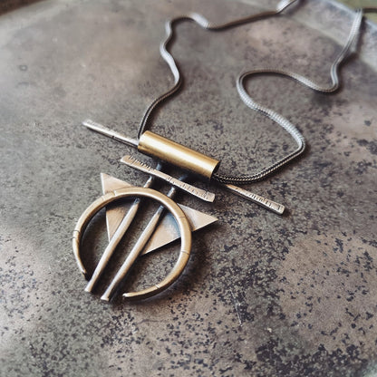 A silver and gold-colored necklace with a geometric pendant, featuring a chain and a series of geometric shaped pendants attached to it.