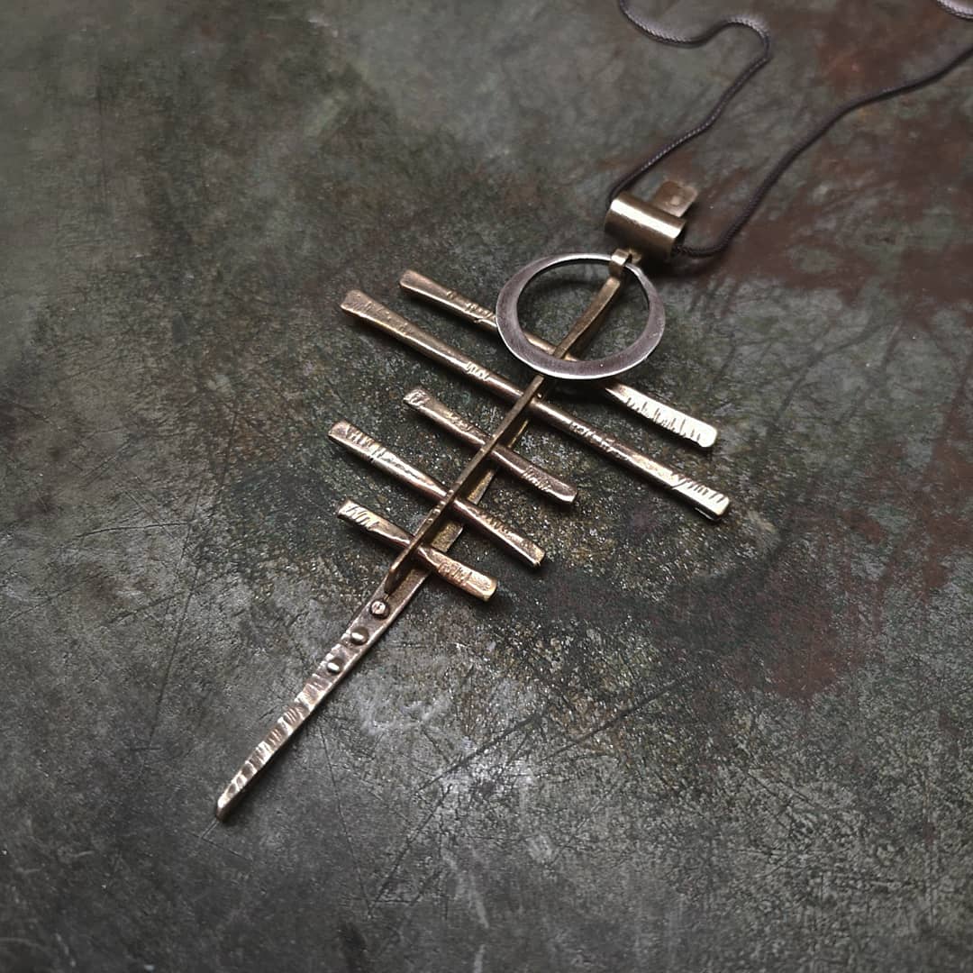 A silver-colored necklace with a pendant featuring a series of parallel lines and a circular ring
