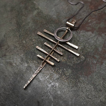 A silver-colored necklace with a pendant featuring a series of parallel lines and a circular ring