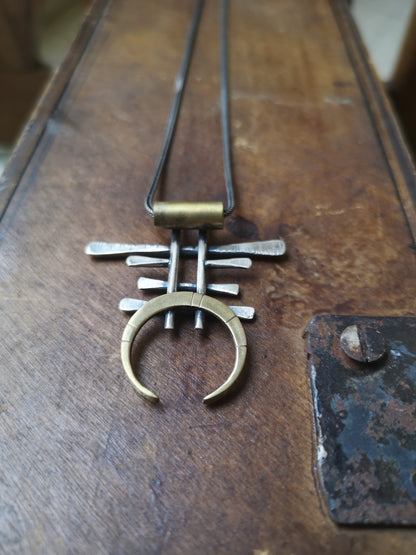 A necklace with a unique geometric pendant made of silver and brass, featuring an oxidized and brushed finish.