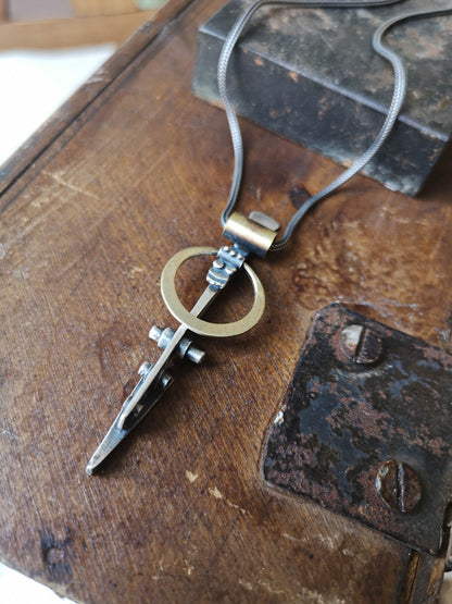 A silver necklace with a pendant featuring a ladder shape and a small cow symbol in the center