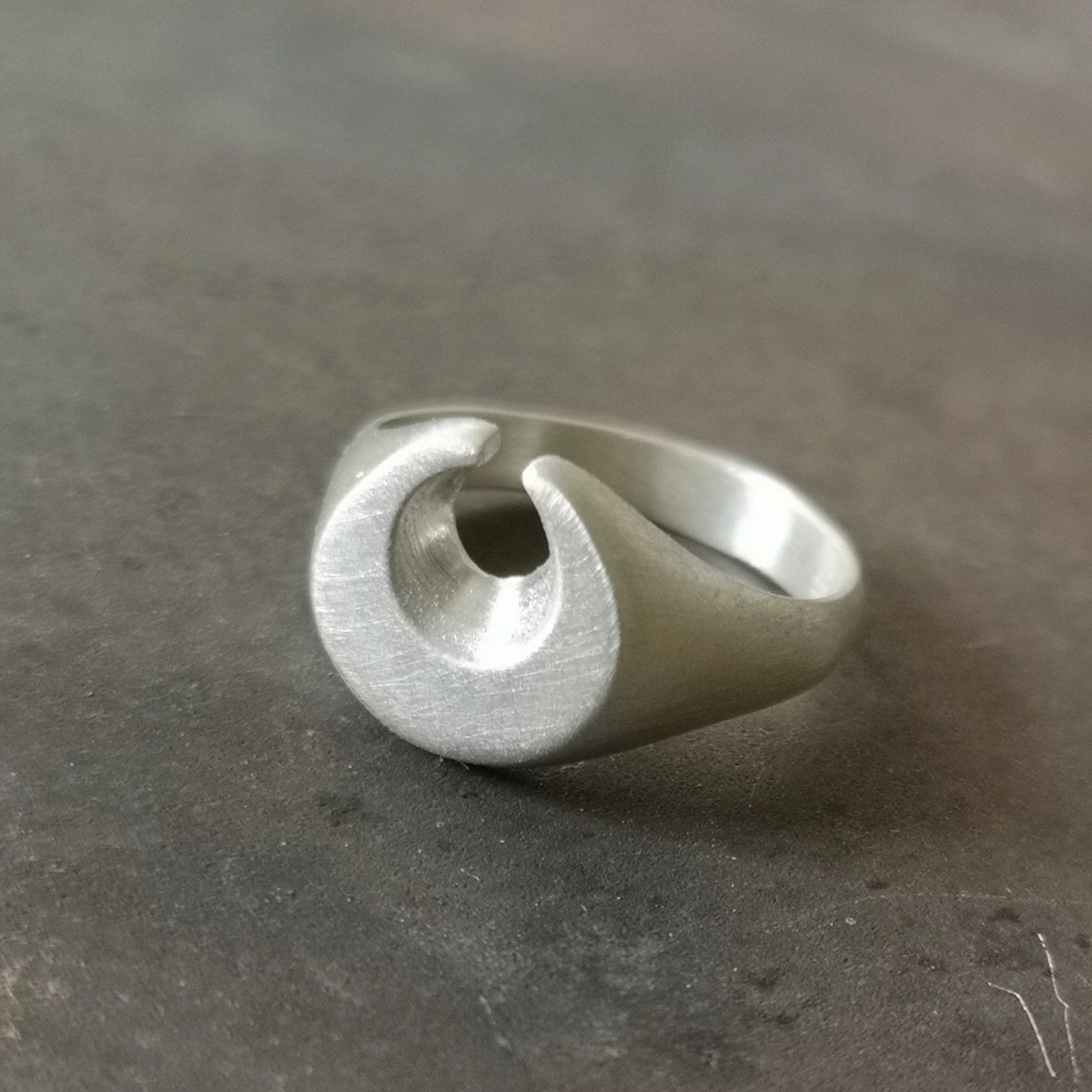 A silver ring featuring a brushed finish, handcrafted in the shape of a moon.