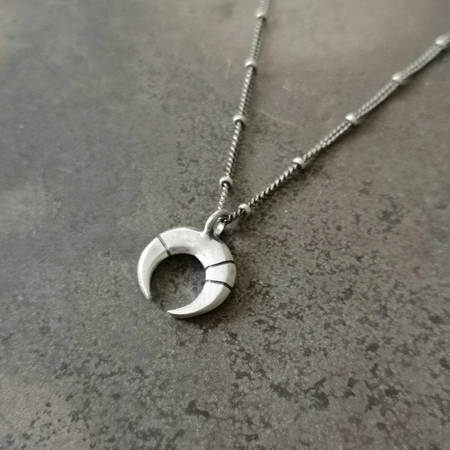 A silver necklace with a crescent-moon pendant and chain.