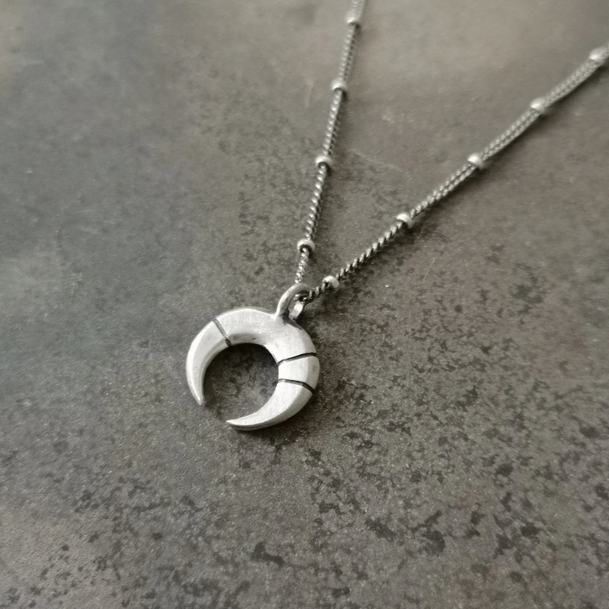 A silver necklace with a crescent-moon pendant and chain.