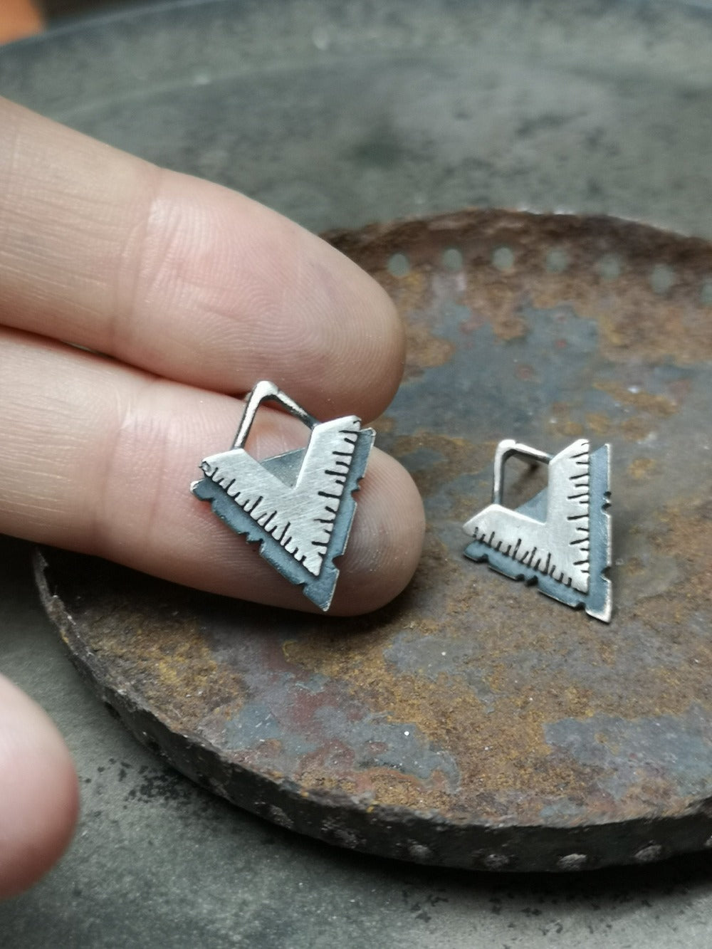 A pair of silver earrings with a geometric design, featuring a triangular shape with lines on the side