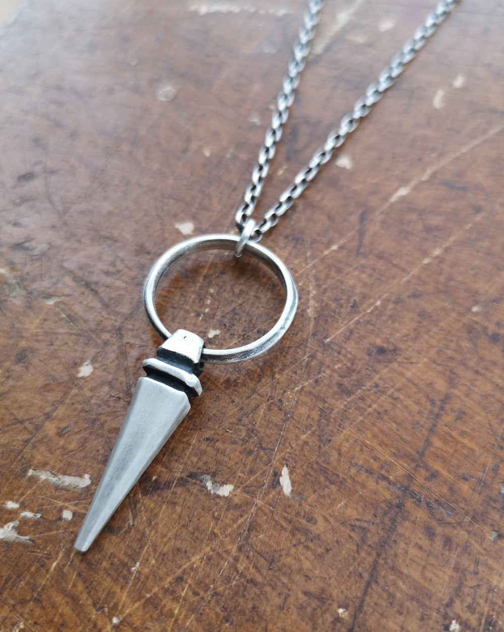 A sterling silver pendulum necklace with a brushed finish and a chain loop at the top. The pendulum is large and has a smooth, polished appearance.