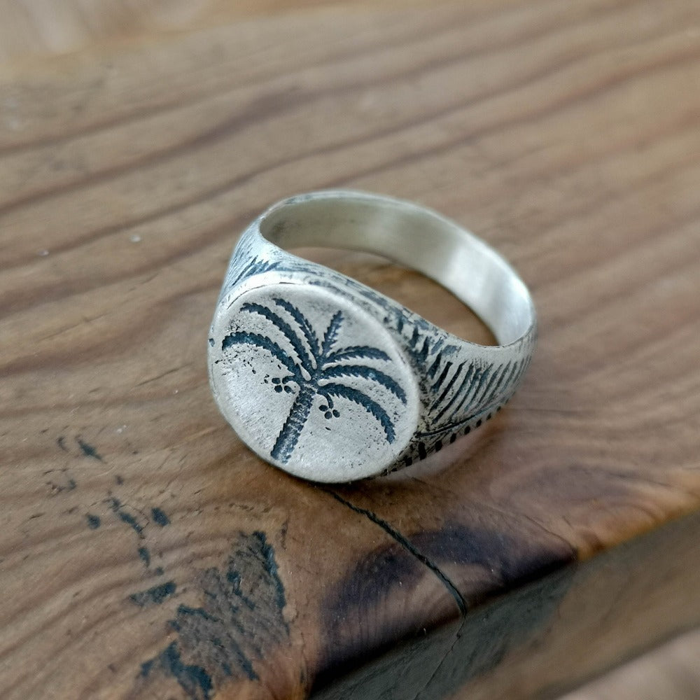 A silver ring with a brushed finish and a palm tree design on the top, signet-style.