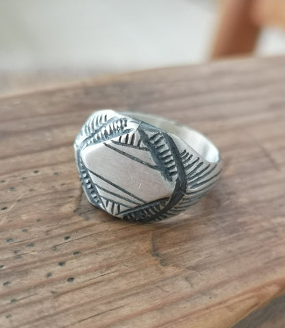 A silver signet ring with a geometric pattern on the top part, surrounded by a plain band.