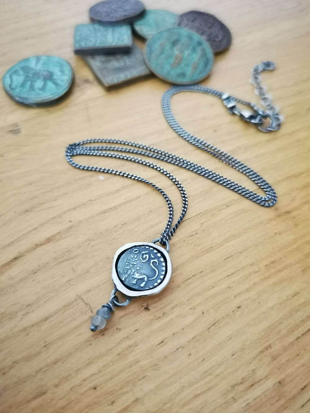 A silver necklace with a pendant featuring an ancient Hindu coin design with the figure of Hanuman- Monkey god, accompanied by two tiny labradorite stones.