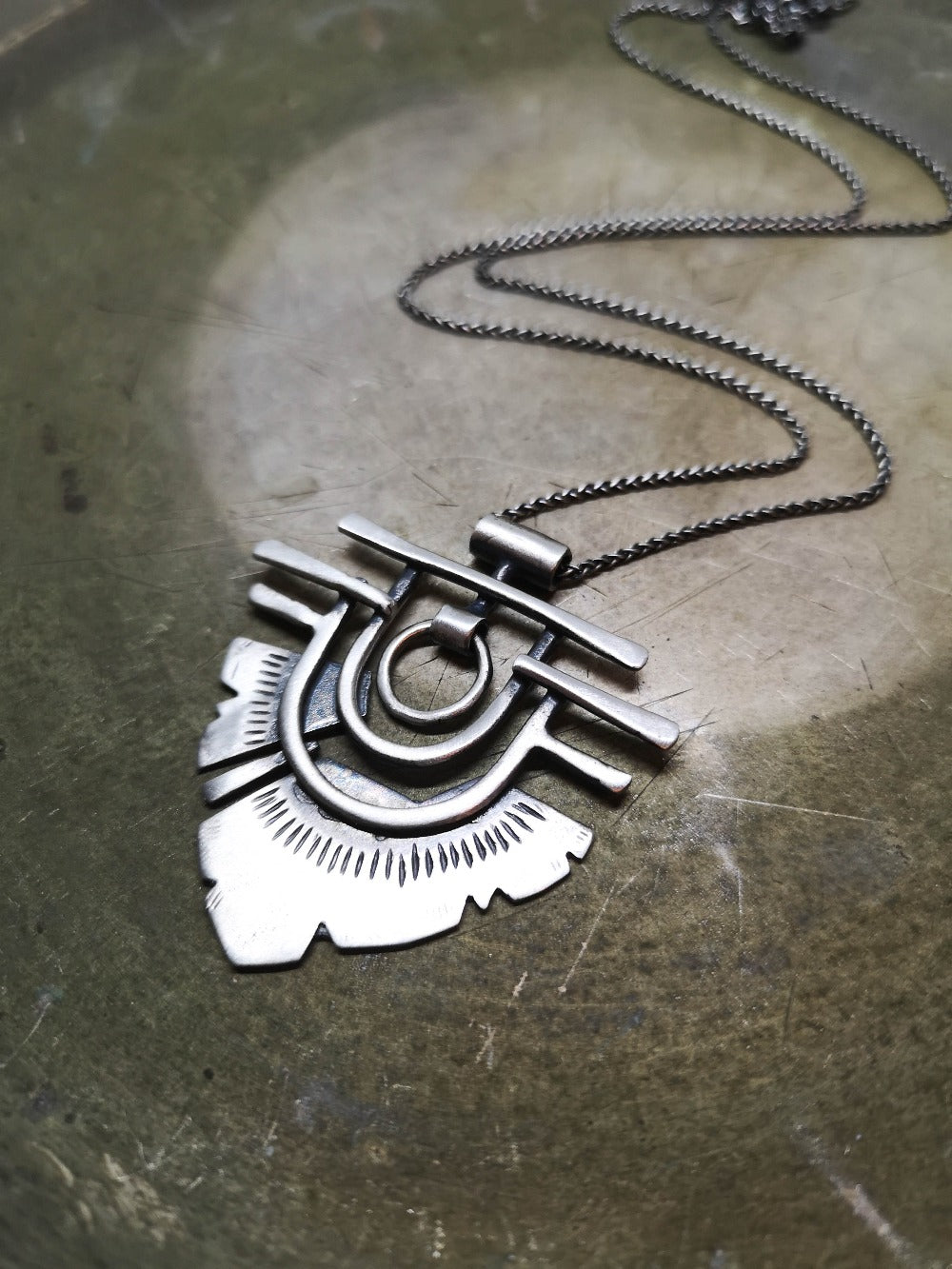 A silver necklace with a geometric-patterned pendant resembling flame 
