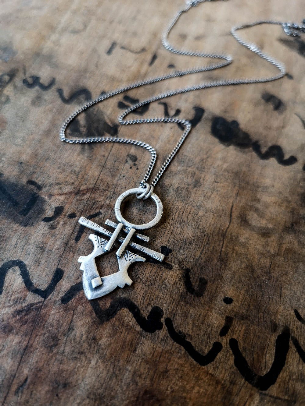 A silver necklace with a pendant featuring a stylized key design, on a wooden background.