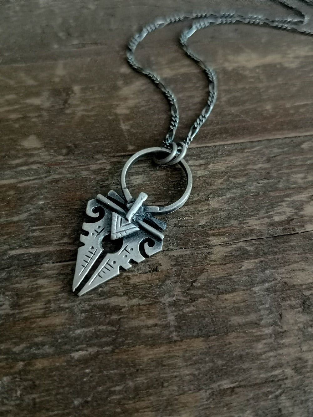 A sterling silver necklace with an oxidized and brushed finish, featuring a pendant with a strength symbol design.