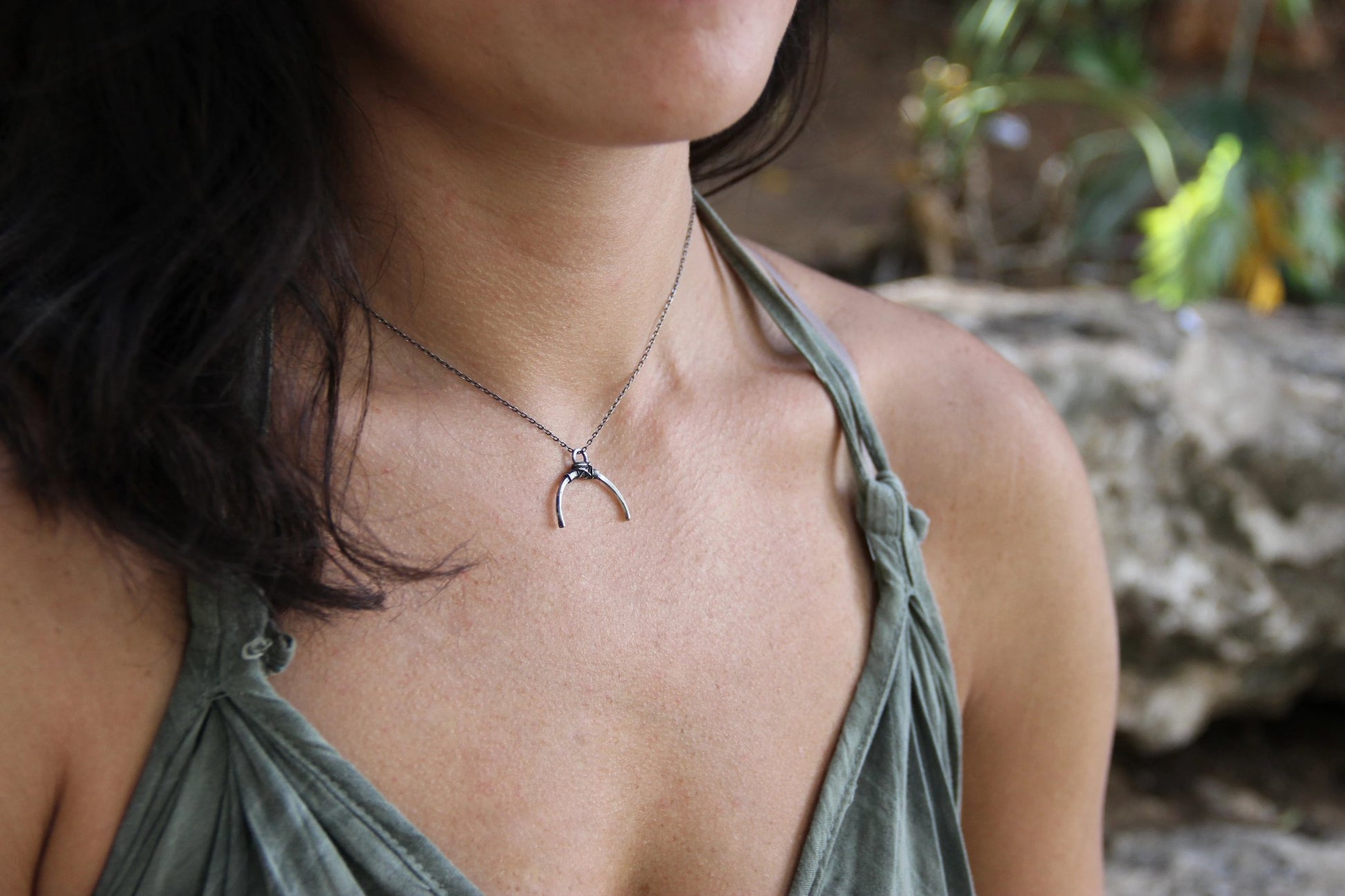A silver necklace with a crescent-shaped pendant, featuring a chain with a series of small bell-like charms attached to it.