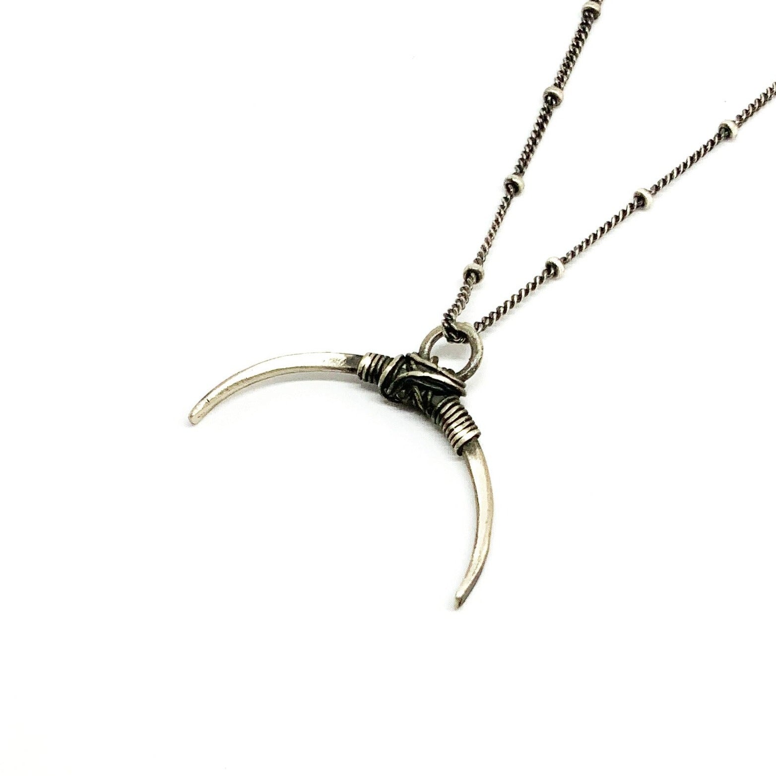 A silver necklace with a crescent-shaped pendant, featuring a chain with a series of small bell-like charms attached to it.