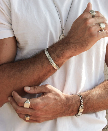 A sterling silver bracelet with an oxidized and brushed finish, featuring text on the bracelet surface.