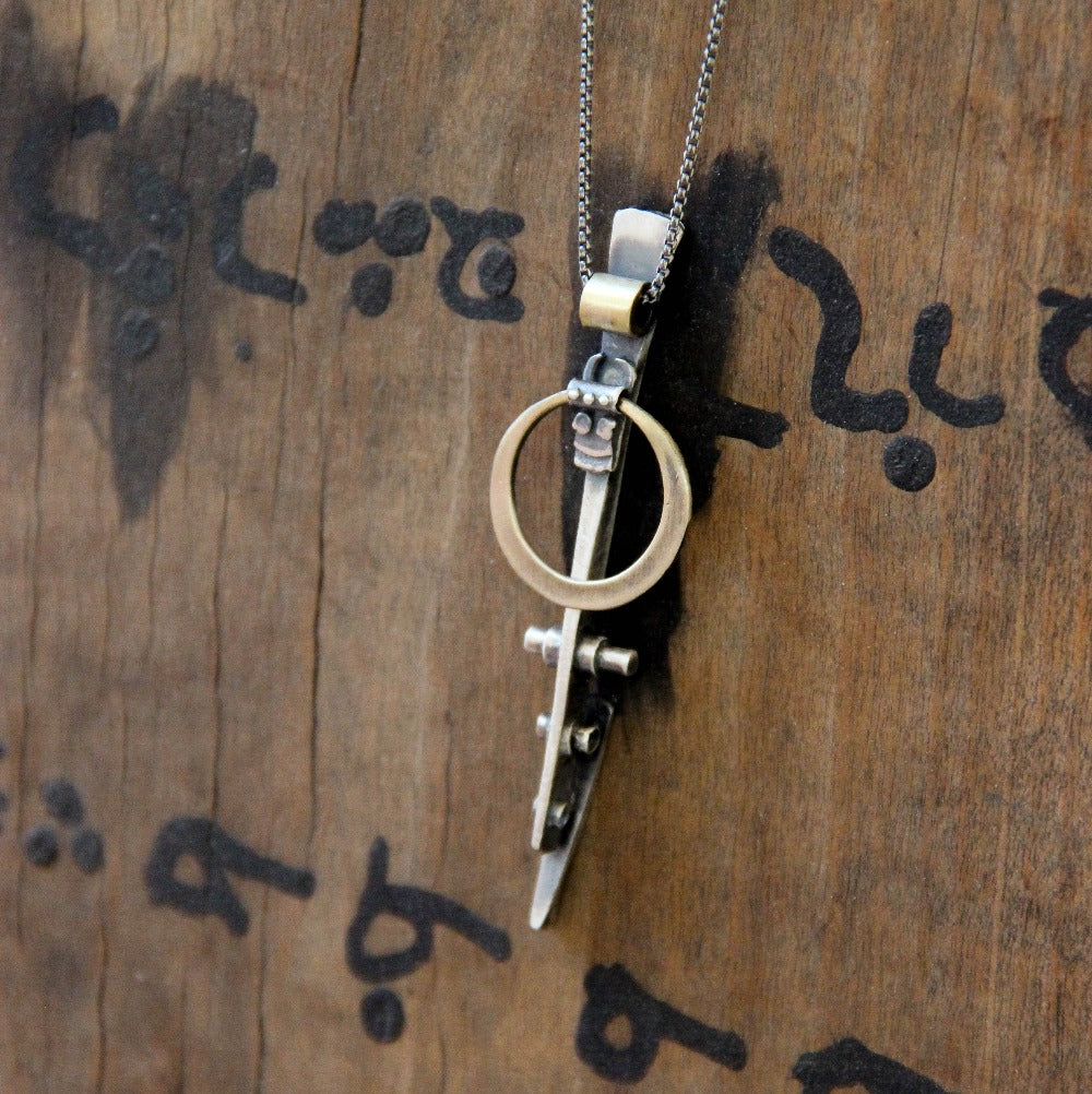 A silver necklace with a pendant featuring a ladder shape and a small cow symbol in the center