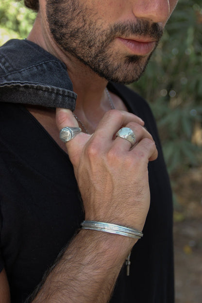 A sterling silver bracelet with an oxidized and brushed finish, featuring text on the bracelet surface.
