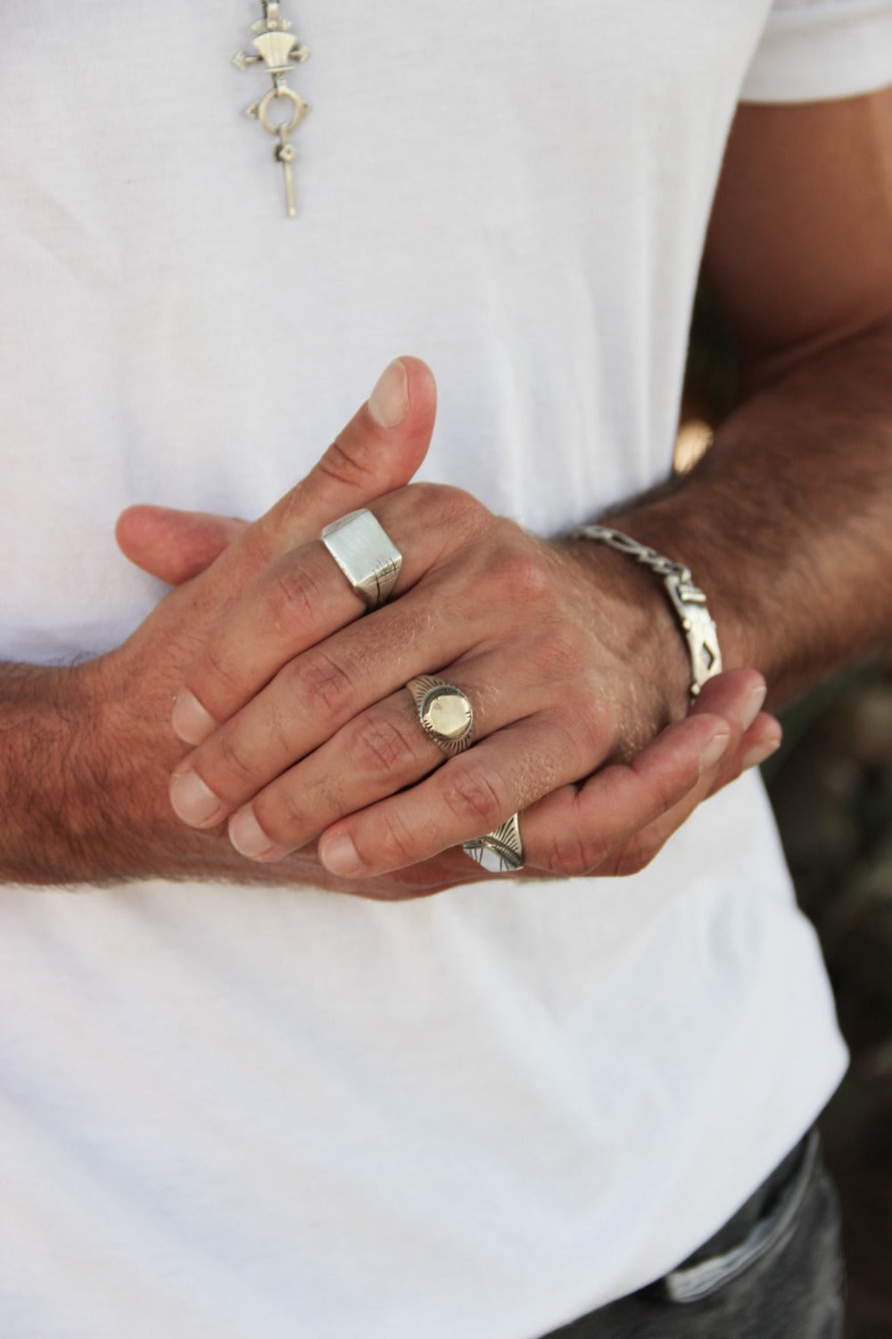 Men wearing silver shelly ganz silver ring with a brushed finish and a central golden brass sun emblem, with engraved patterns around it. lotus necklace and a silver bracelet
