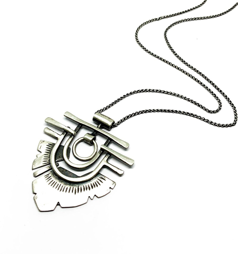 A silver necklace with a geometric-patterned pendant resembling flame 