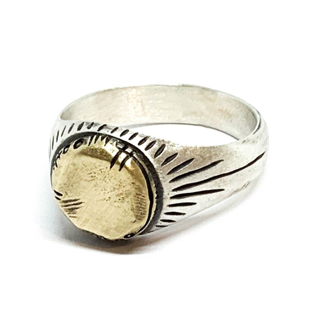 A silver ring with a brushed finish and a central golden brass sun emblem, with engraved patterns around it.