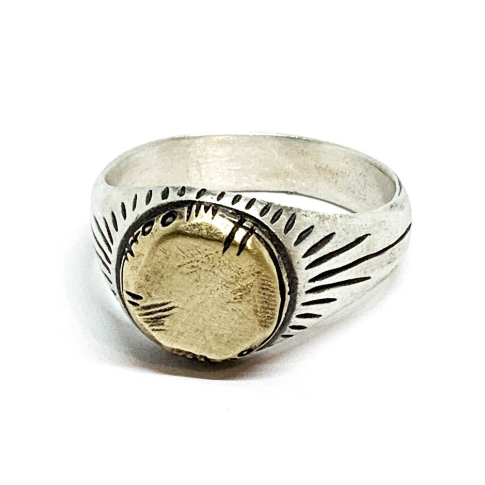 A silver ring with a brushed finish and a central golden brass sun emblem, with engraved patterns around it.