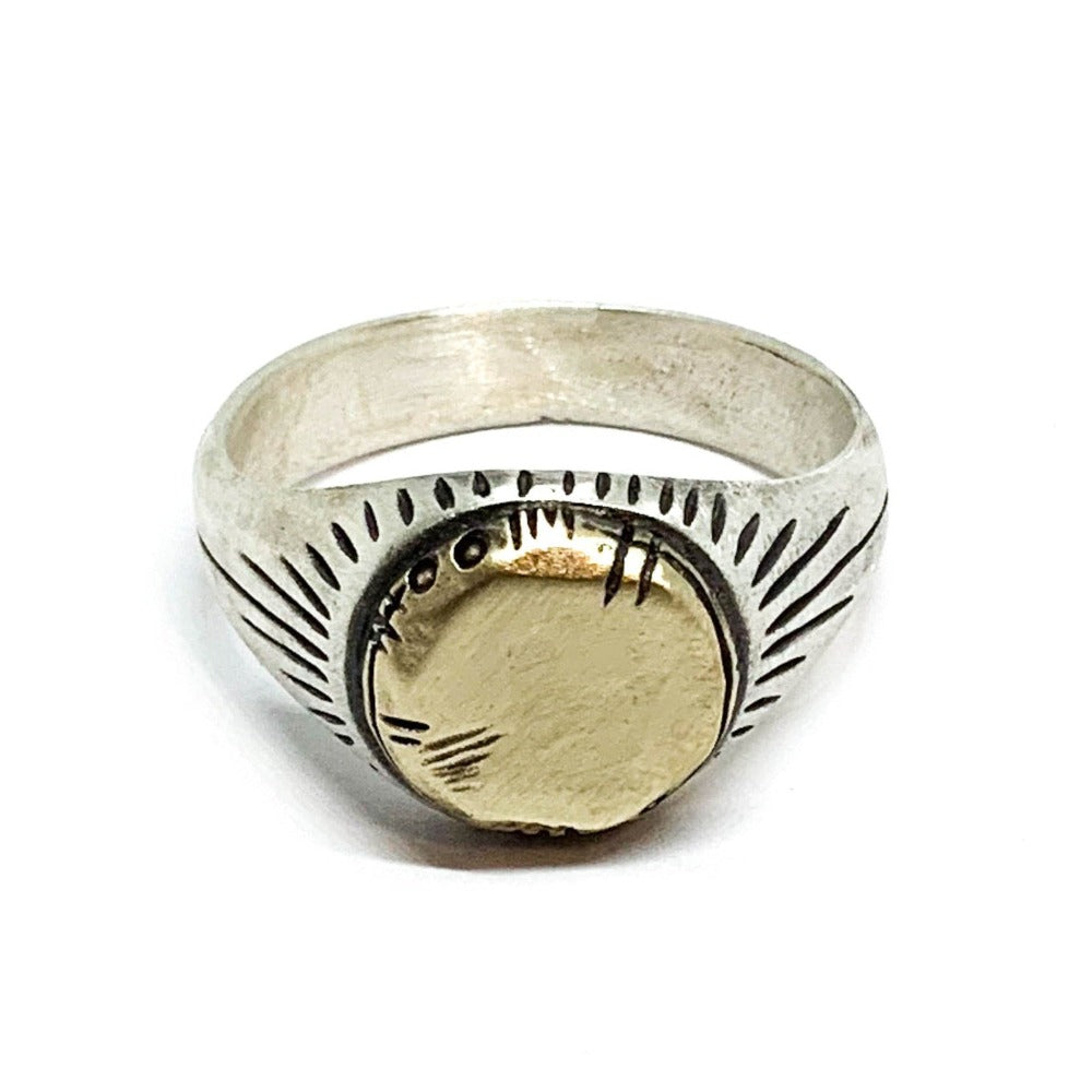 A silver ring with a brushed finish and a central golden brass sun emblem, with engraved patterns around it.
