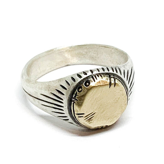 A silver ring with a brushed finish and a central golden brass sun emblem, with engraved patterns around it.