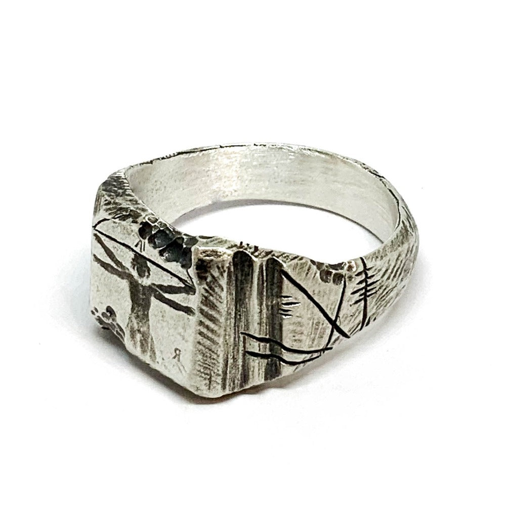 A silver ring with an oxidized and brushed finish, featuring an engraved design inspired by Florentine art, including figures and architectural elements.