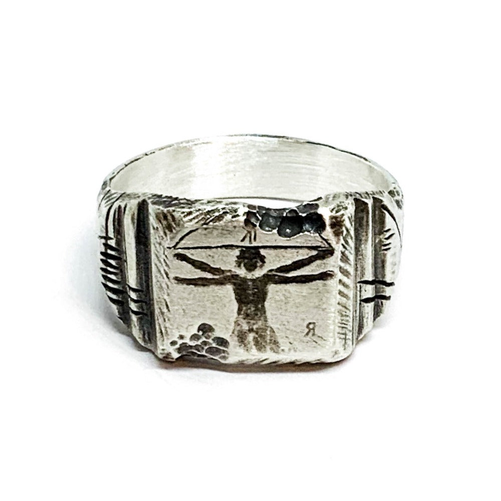 A silver ring with an oxidized and brushed finish, featuring an engraved design inspired by Florentine art, including figures and architectural elements.