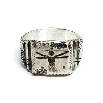 A silver ring with an oxidized and brushed finish, featuring an engraved design inspired by Florentine art, including figures and architectural elements.