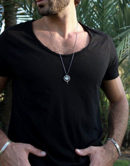 A silver necklace with a pendant featuring a circular design and a chain that ends in a pendant loop.