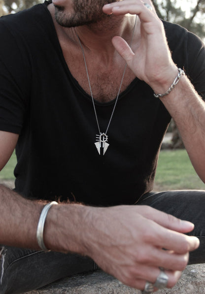A sterling silver necklace with a pendant featuring two triangles and a circular ornament, with a brushed and oxidized finish.