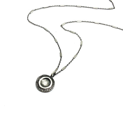 A silver necklace with a pendant featuring a stylized sun and moon design, on a white background.