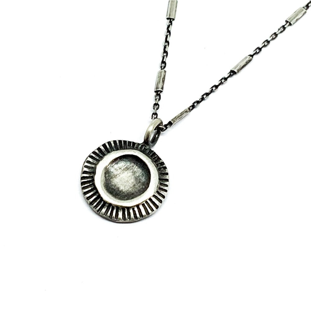 A silver necklace with a pendant featuring a stylized sun and moon design, on a white background.