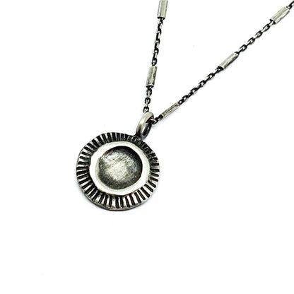 A silver necklace with a pendant featuring a stylized sun and moon design, on a white background.