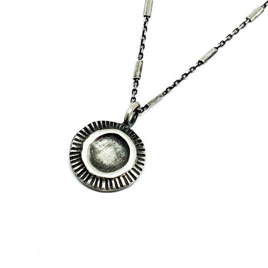 A silver necklace with a pendant featuring a stylized sun and moon design, on a white background.