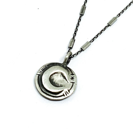 A silver necklace with a pendant featuring a stylized sun and moon design, on a white background.