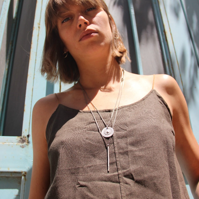 A silver necklace with a pendant featuring a circular design and a chain that ends in a pendant loop.