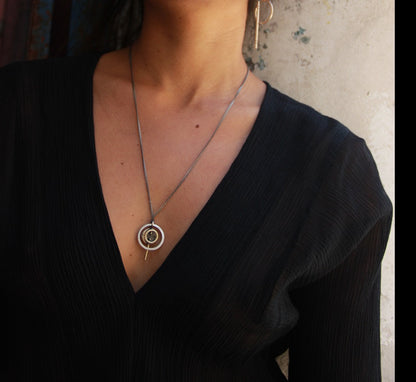 A silver necklace with a pendant featuring a circular design and a chain that ends in a pendant loop.