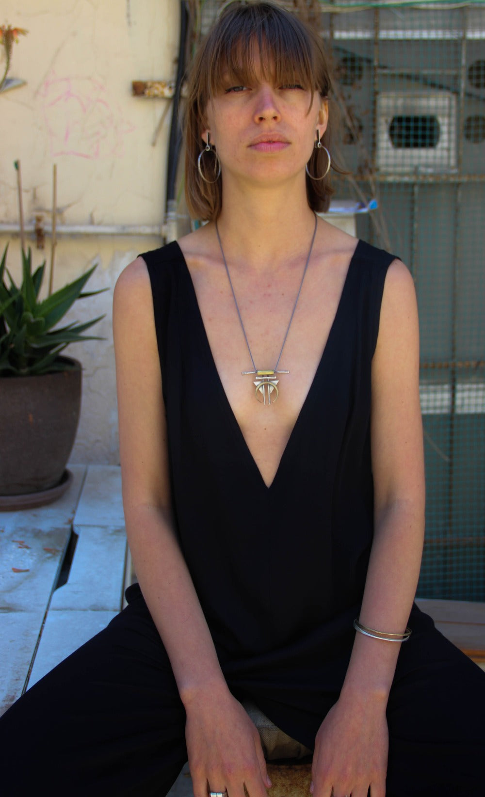 A silver and gold-colored necklace with a geometric pendant, featuring a chain and a series of geometric shaped pendants attached to it.