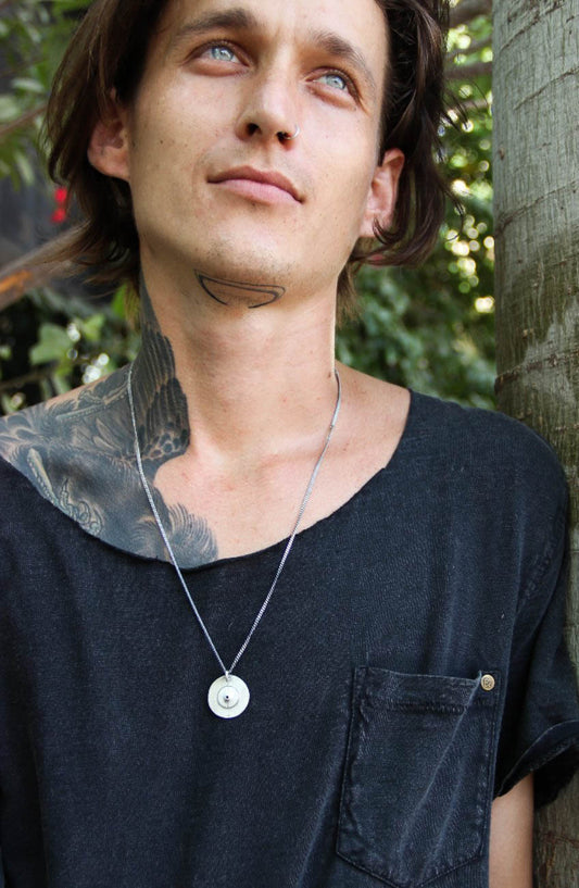 A silver necklace with a pendant featuring a circular design and a chain that ends in a pendant loop.