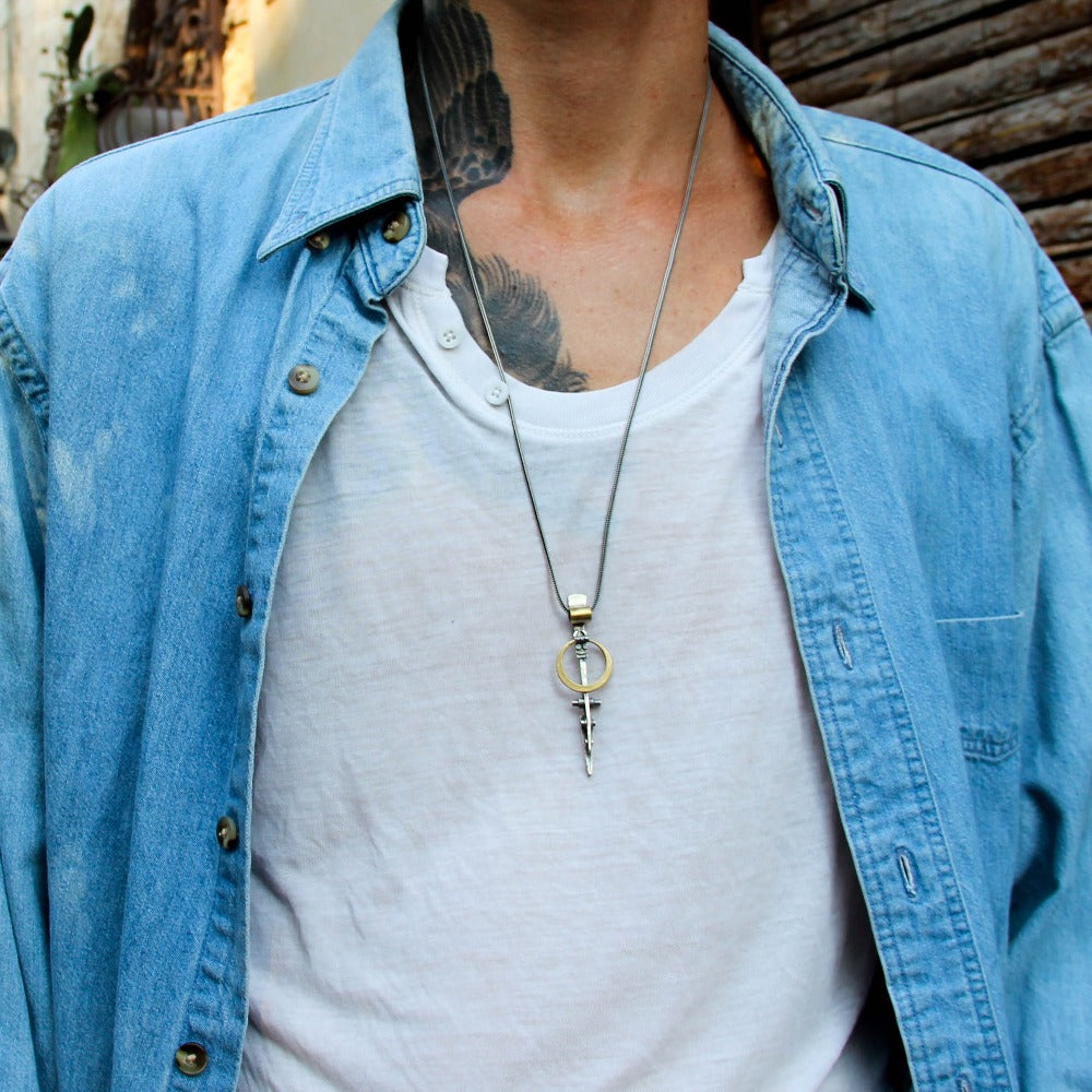 A silver necklace with a pendant featuring a ladder shape and a small cow symbol in the center, against a white background.