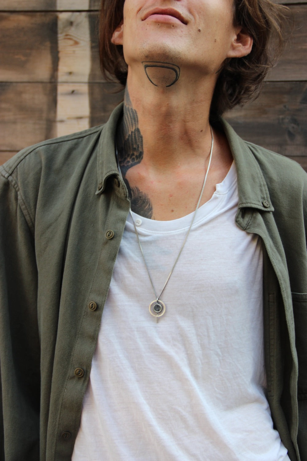 A silver necklace with a pendant featuring a circular design and a chain that ends in a pendant loop.