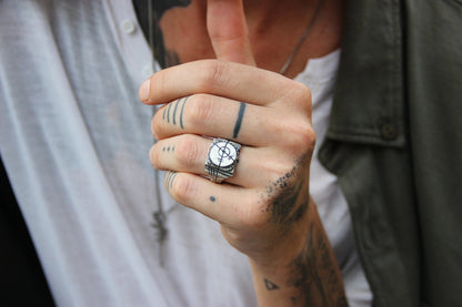 A silver ring with an oxidized and brushed finish, featuring a target design and ornamental details.