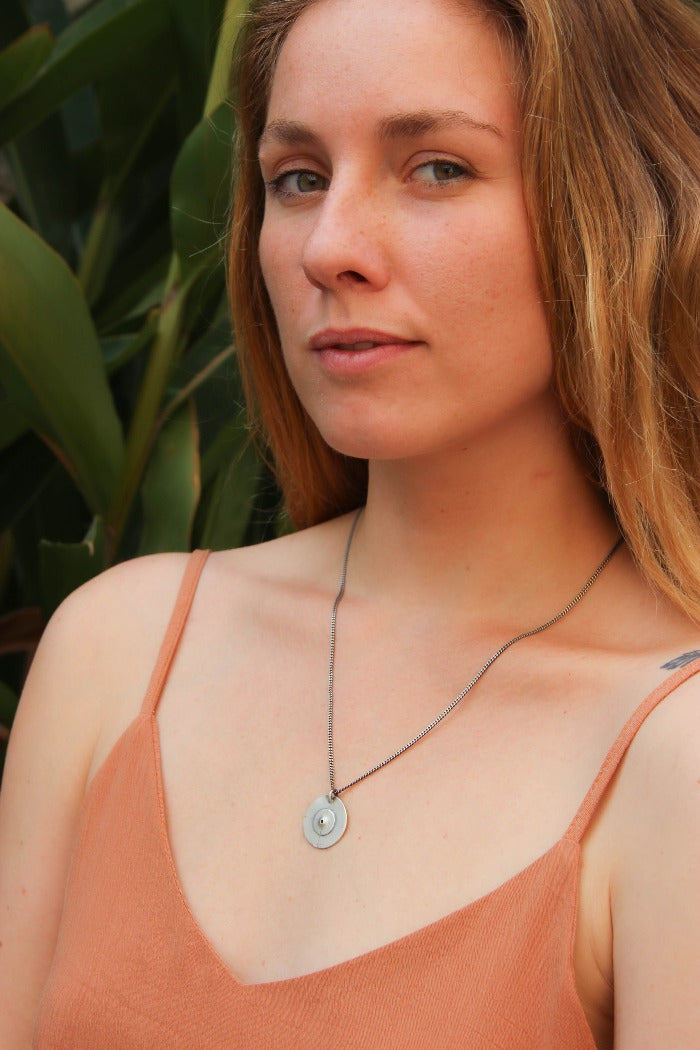 A silver necklace with a pendant featuring a circular design and a chain that ends in a pendant loop.