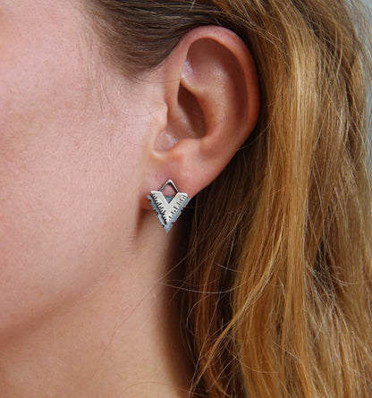 A pair of silver earrings with a geometric design, featuring a triangular shape with lines on the side