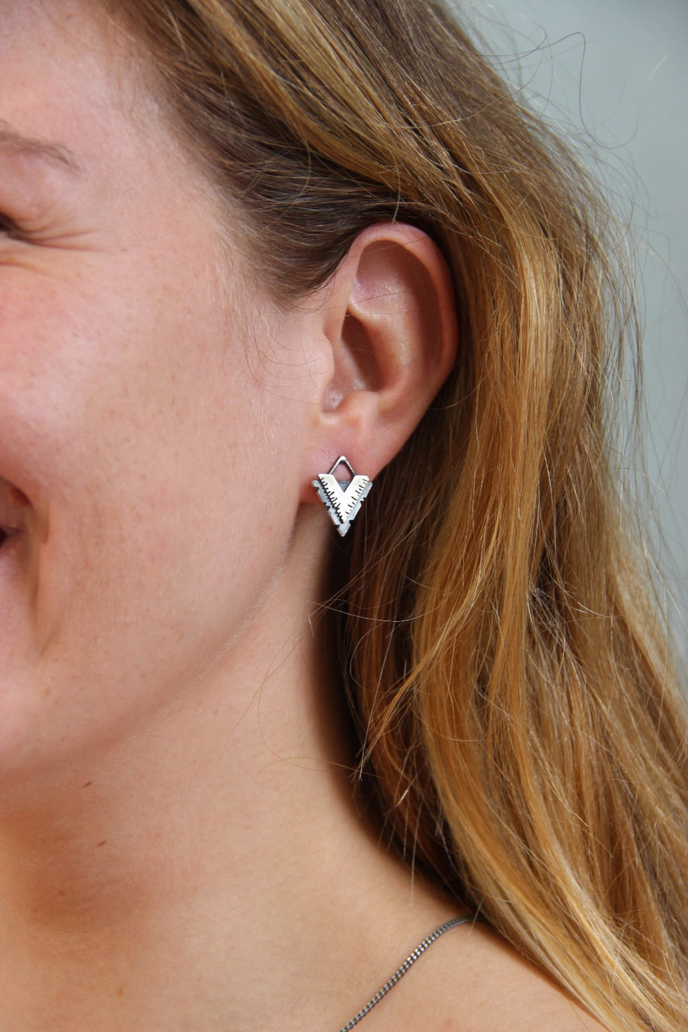 A pair of silver earrings with a geometric design, featuring a triangular shape with lines on the side