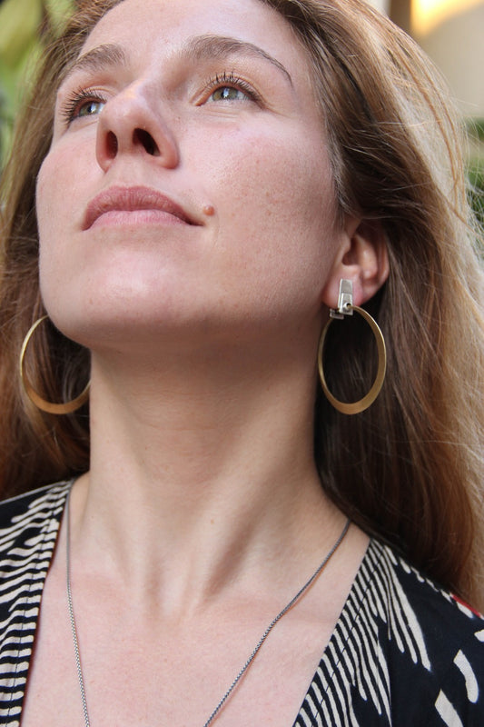 A pair of silver and brass hoop earrings with a brushed finish and a geometric design