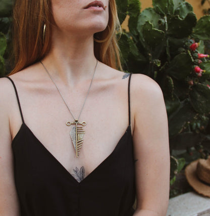 A sterling silver and brass necklace with a pendant featuring a design that resembles an arrow, attached to a chain.