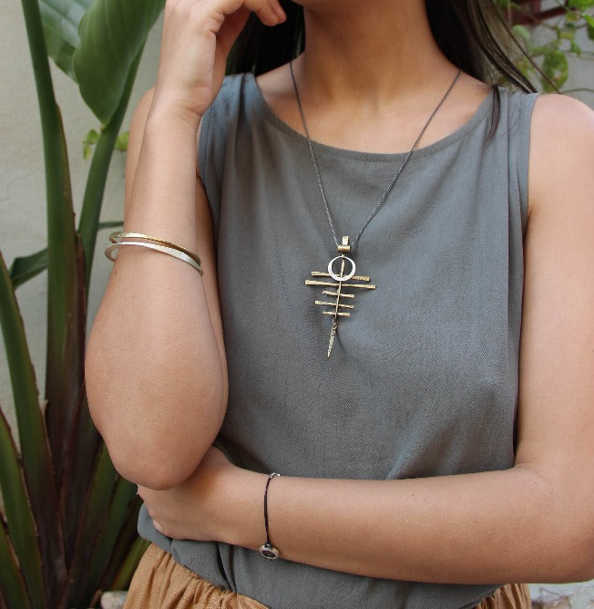 A silver-colored necklace with a pendant featuring a series of parallel lines and a circular ring